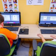 Two children working on computers, learning financial literacy skills, in the library.