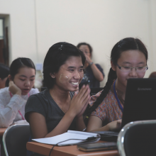 Smiling students learning to use computers in University of Yangon.