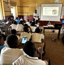 A librarian teaches school students in a school classroom online safety skills, using a whiteboard and projector for slides.