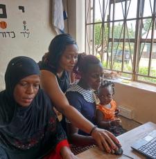 Women learning to use computers at a previous ICT camp in Uganda. One of the women has a baby on her lap.