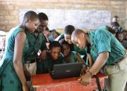 Children in a school classroom crowded around a laptop computer. 