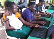 A young woman learning computer skills, with a baby on her shoulder.