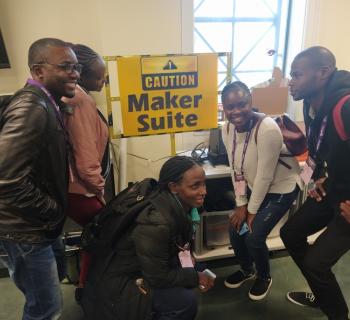 Five young African librarians in a library maker space in Nashville, USA, posing in front of a sign saying - Caution! Maker Suite.