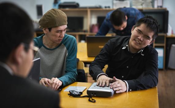 Blind and visually impaired students in Ulaanbaatar, Mongolia, work with digital audio equipment. Two young men sitting at a library desk working with new Daisy players. The instruction booklet is on the desk.