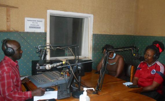 Nakaseke Radio studio, with a presenter at the mixing desk and two people in the studio. 
