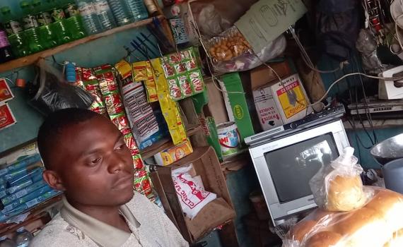 Martin Kakuru in his store, with a screen and bread he has baked, ready to sell.