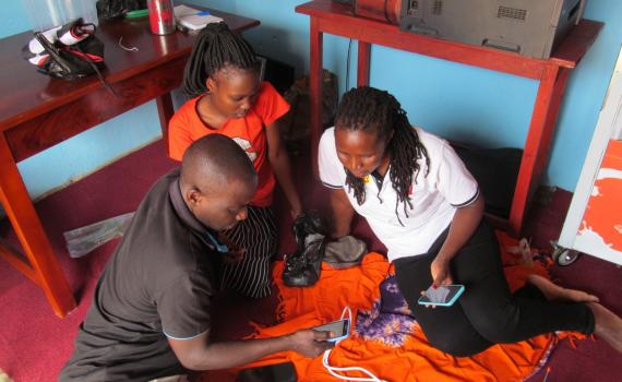 Peter Balaba, librarian at Nakaseke Public Library teaches two women how to use the internet on their smartphones.