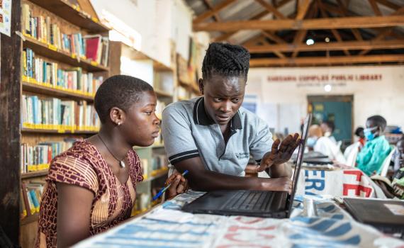 A teacher showing a young women how to use a computer in Caezxaria Public Library in Uganda.