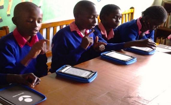 Children at a desk using kindles to read 