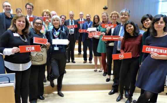 Group photo of 19 representatives from library, archive, museum and education sectors at SCCR/37. They are standing in a long line down a shallow stairs in the WIPO conference hall, holding organization name plaques.